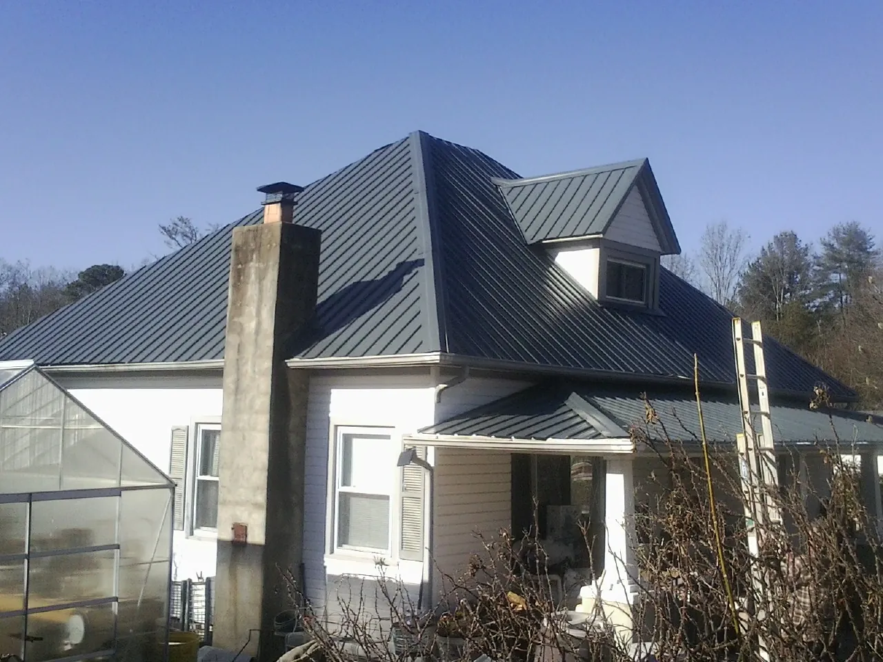 Dark blue standing seam metal roof on a white farmhouse with dormer — Slate & Tile Roof Repair by Roofing Brothers in Cambria Heights