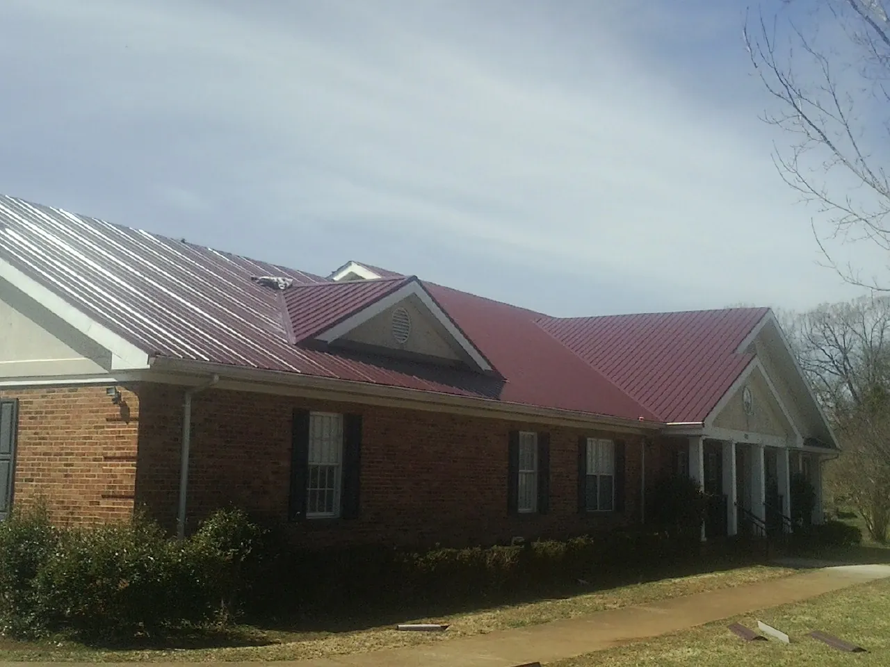 Red metal roof with gabled entries on a long brick building, from a Hail Damage Roof Repair job in Cambria Heights