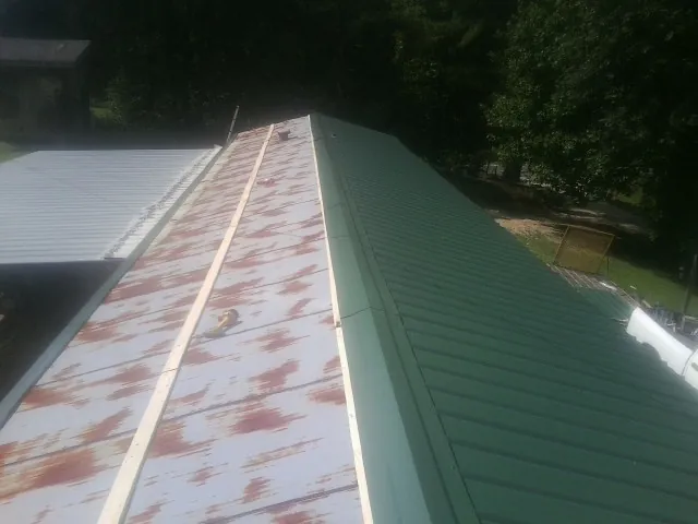 Old rusted panels beside newly installed green metal roofing — Wind Damage Roof Repair by Roofing Brothers in Cambria Heights