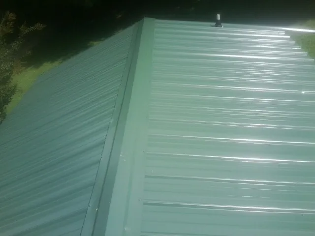 New green metal panels meeting at the ridge of a roof — Flat Roof Repair work by our crew in Cambria Heights