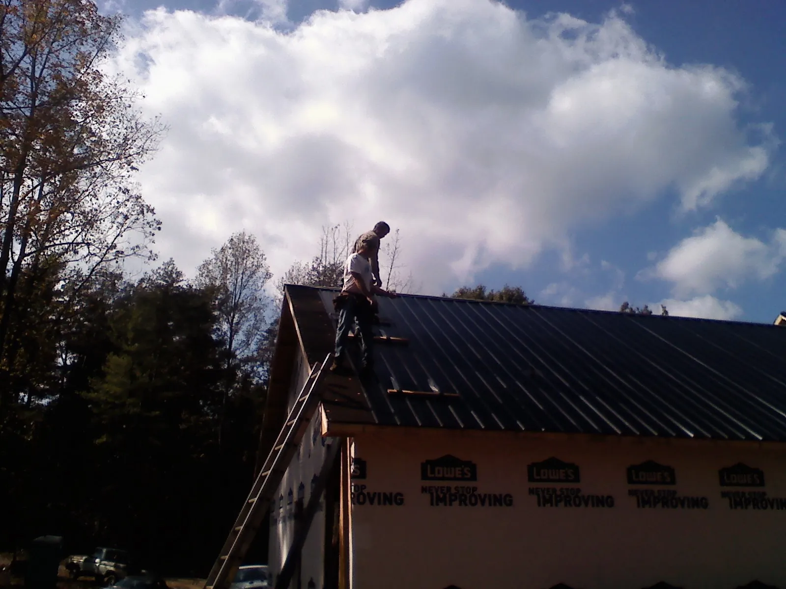 Roofer fastening dark metal panels high against a cloudy sky, from a Roof Inspection job in Cambria Heights