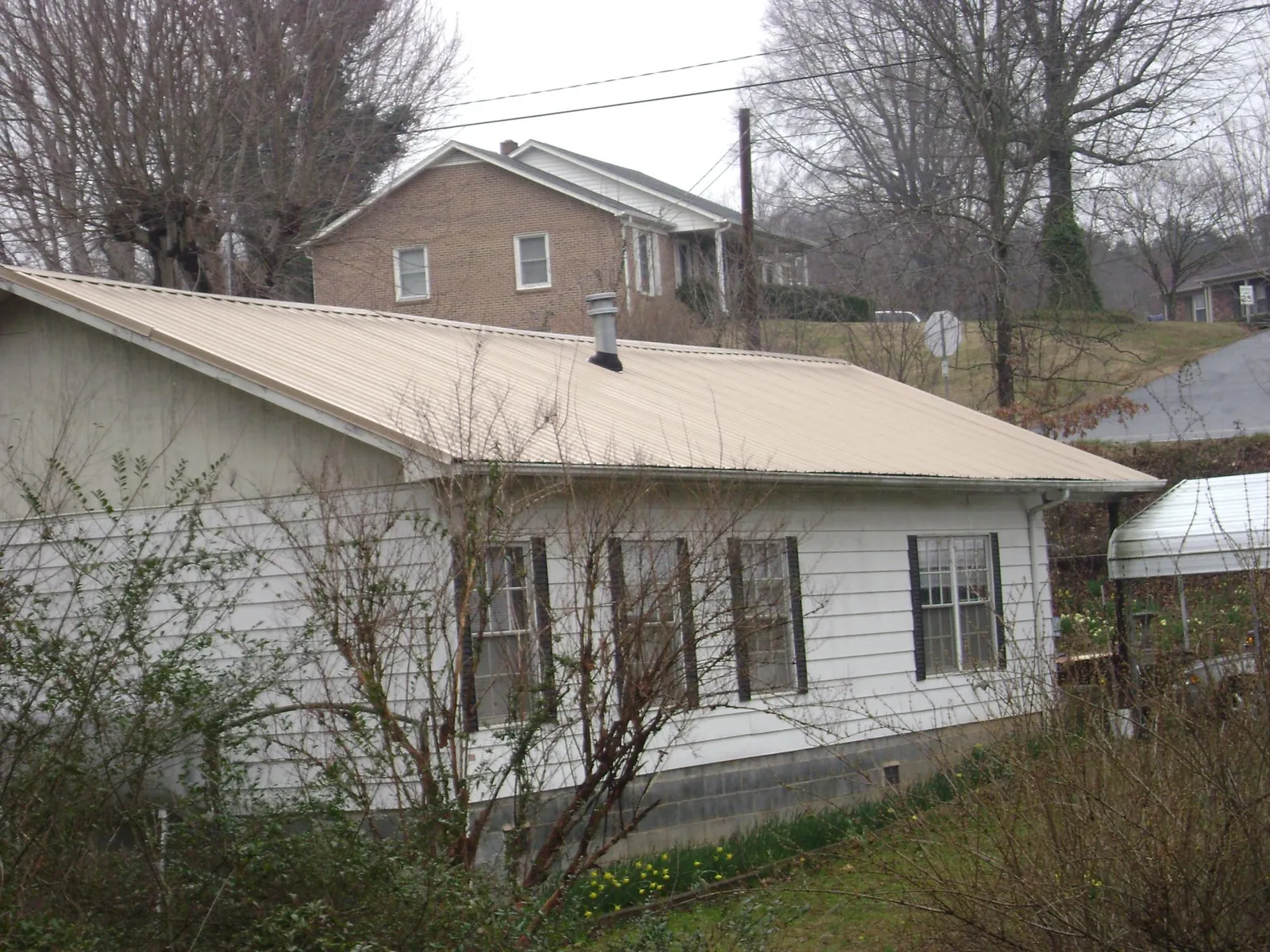 Tan metal roof on a white sided house set into a hillside — Commercial Roofing by Roofing Brothers in Cambria Heights