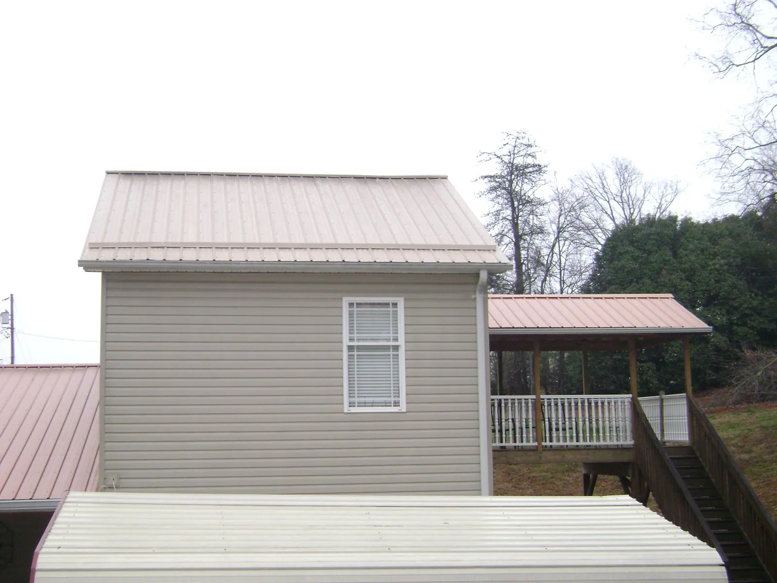 Tan metal roofs on a two story addition and attached porch, from a Roof Replacement job in Cambria Heights