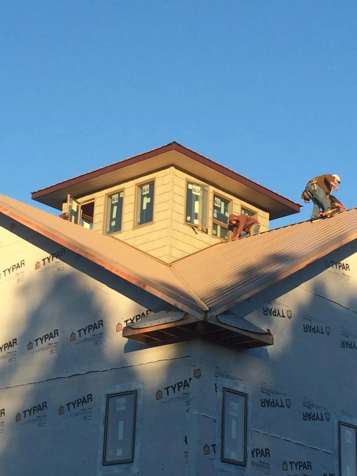 Roofers working around a rooftop cupola on a new metal roof at sunset — Roof Waterproofing in Cambria Heights by Roofing Brothers